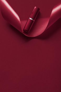 Cosmetic branding, glamour lip gloss and shopping sale concept - Luxury lipstick and silk ribbon on maroon holiday background, make-up and cosmetics flatlay for beauty brand product design