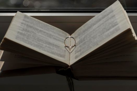 Wedding ring with a falling shadow in the form of a heart standing on an open book...