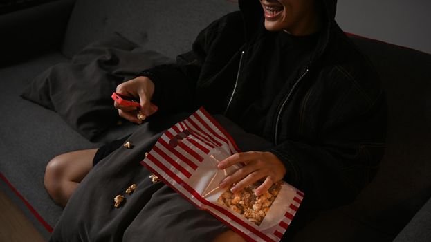 Happy man with remote control eating popcorn and watching movie in living room. Entertainment and leisure activity concept.