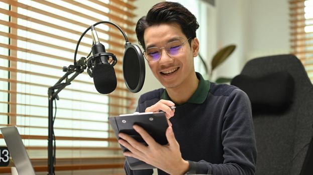 Young podcaster using a microphone and laptop computer recording audio for channel in home studio.