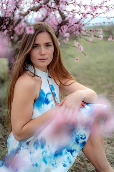 Young beautiful woman in blue dress and long hair is enjoying with blossoming peach trees.