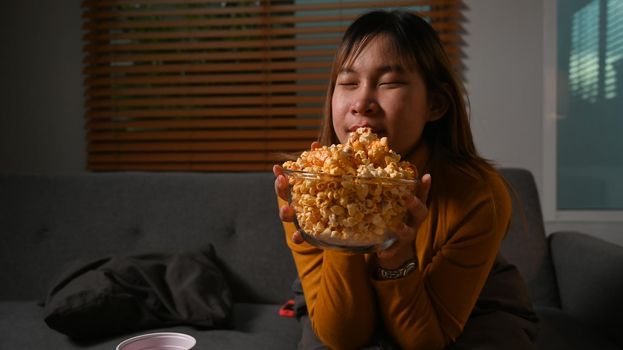 Smiling young woman enjoy eating popcorn and watching movie at home. Entertainment and leisure activity concept.