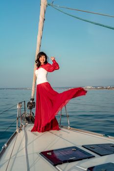 Attractive middle-aged woman in a red dress on a yacht on a summer day. Luxury summer adventure, outdoor activities