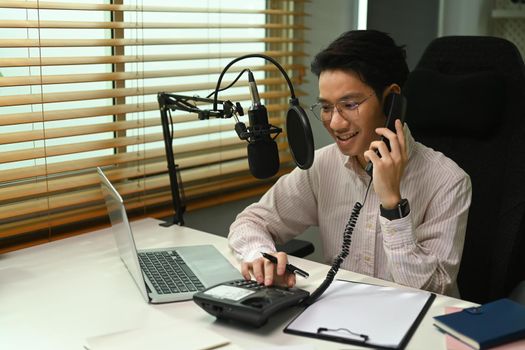 Young podcaster using a microphone and laptop computer recording audio for channel in home studio.