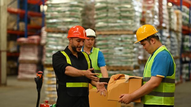 Warehouse workers in safety uniform working in warehouse full of tall shelves with goods in cardboard boxes.