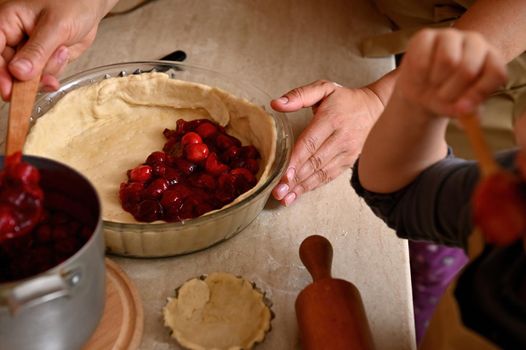 Selective focus: Glass mold with rolled out pastry dough, filled with caramelized cherries. Baking homemade tartlets, cake, pie according to traditional family recipe. Festive baked pastries. Close-up