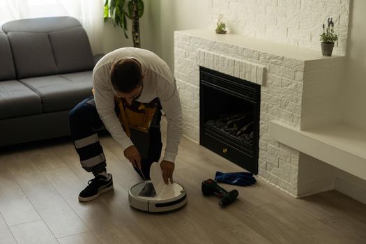 Housework and technology concept. Maintenance and service of robot vacuum cleaner. Cleaning, repair, replacement of parts. Man repairing robot cleaner at home. Smart home functions, fully automated.
