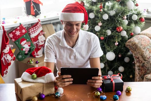 man at home christmas with santa claus hat with tablet.
