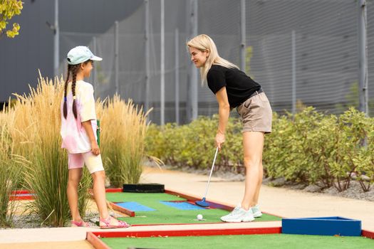 Mother playing with her cute daughter mini golf at outdoor playground