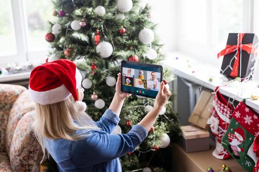 Woman with santa hat using video call conference on tablet, decorations and lights at home. Caucasian adult for christmas eve party.