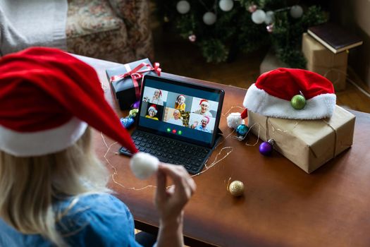 A middle-aged blonde woman uses a tablet for a video call while sitting in an armchair.