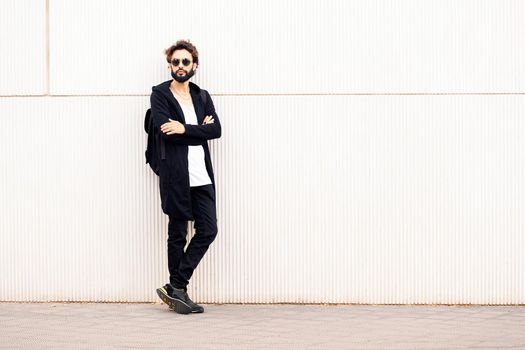 beautiful young man with sunglasses leaning in a white wall, concept of urban lifestyle and stylish clothing, copy space for text