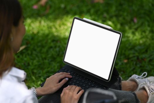 Young woman sitting on green grass in the nature park and working with digital tablet.