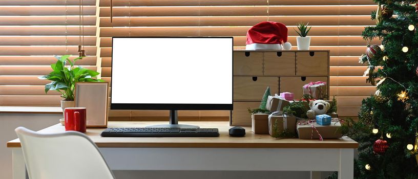 Mock up computer with white display, houseplant and Christmas gifts on wooden table.