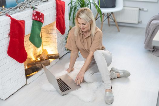 Nice beautiful blonde lady works at the notebook sit down on the sofa at home - check on oline shops for cyber monday sales - technology woman concept for alternative office freelance.