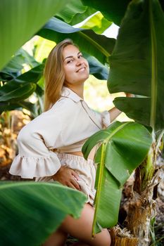 Woman near green leaves of banana bushes on nature in a park in a tropical place, she is in a beige skirt and a blouse