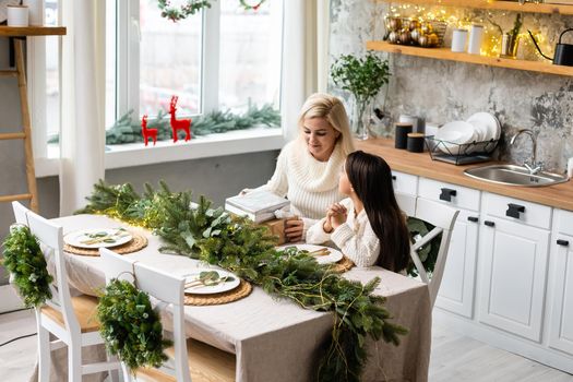 Beautiful mother and daughter have fun, hug and kiss at home near the Christmas tree in a white interior. Family happiness, holiday, joy, vacation, games with a woman. New Year's preparations.