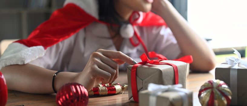 Young woman decorating Christmas presents in living room.