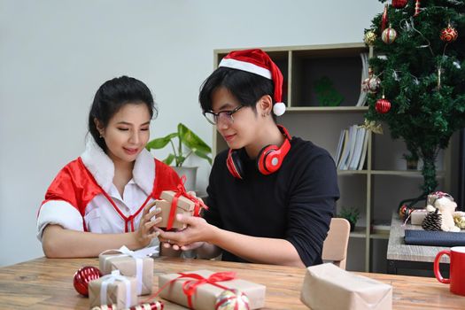 Happy young couple opening Christmas gift in living room at Christmas time.