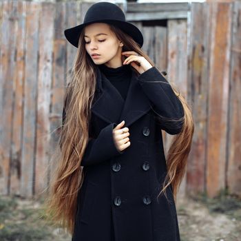 Young beautiful fashionable woman in black hat, with long hair posing on woody background. Female fashion, beauty concept. Outdoor.