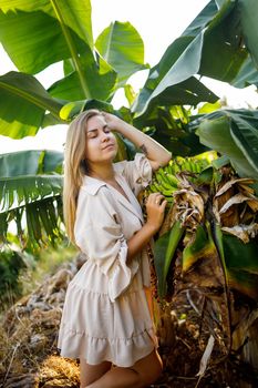 Woman near green leaves of banana bushes on nature in a park in a tropical place, she is in a beige skirt and a blouse