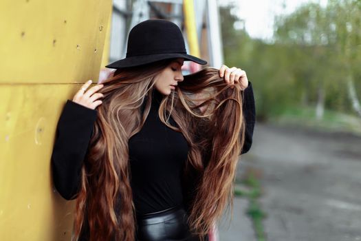 Young beautiful fashionable woman in black hat, with long hair posing on blurry background. Female fashion, beauty concept. Outdoor.