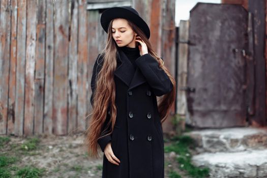 Young beautiful fashionable woman in black hat, with long hair posing on woody background. Female fashion, beauty concept. Outdoor.