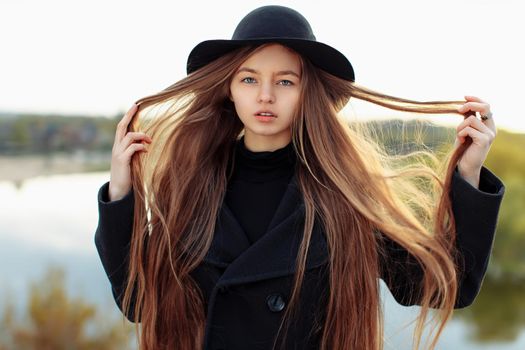 Close-up portrait of young beautiful fashionable woman in black hat, with long hair. Female fashion, beauty concept. Outdoor.