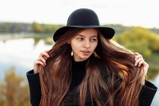 Close-up portrait of young beautiful fashionable woman in black hat, with long hair. Female fashion, beauty concept. Outdoor.