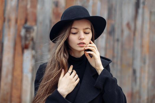 Young beautiful fashionable woman in black hat, with long hair posing on woody background. Female fashion, beauty concept. Outdoor.