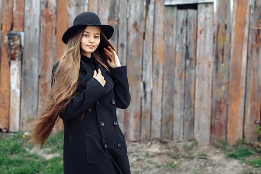 Young beautiful fashionable woman in black hat, with long hair posing on woody background. Female fashion, beauty concept. Outdoor.