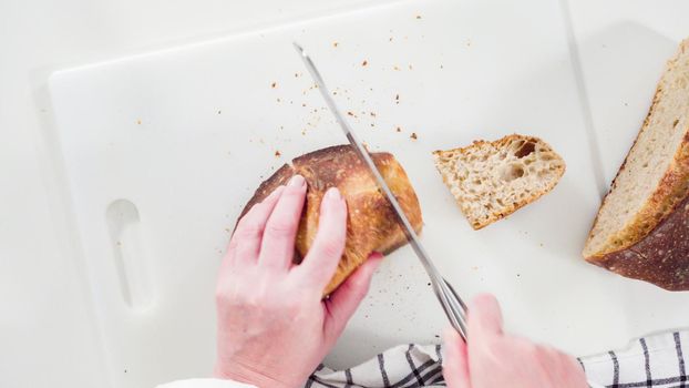 Flat lay. Slicing freshly baked sourdough wheat bread on a white cutting board.