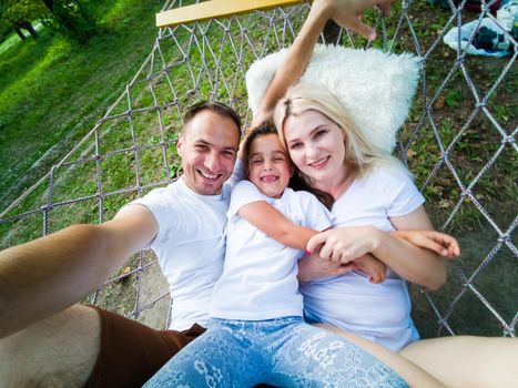 family laying down and relaxing together on a hammock during a sunny summer day on holiday home garden. Family relaxing outdoors, healthy and wellness lifestyle