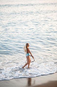 Beautiful girl in a blue swimsuit and hat on a sandy beach at the sea in the sunset sunlight