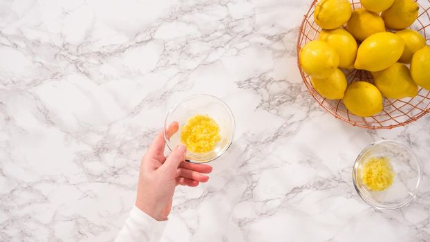 Flat lay. Step by step. Zesting fresh lemons into a glass mixing bowl to prepare lemon bundt cake.