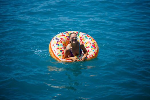 Beautiful young woman in the sea swims on an inflatable ring and has fun on vacation. Girl in a bright swimsuit at the sea under the sunlight