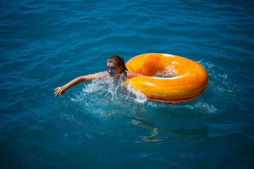 Beautiful young woman fell from an inflatable circle into the blue sea. Girl on vacation swims with a circle on the sea