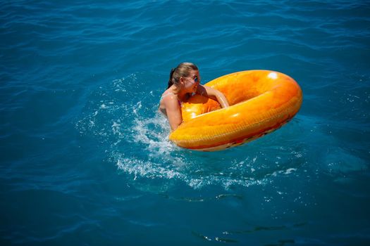 Beautiful young woman fell from an inflatable circle into the blue sea. Girl on vacation swims with a circle on the sea