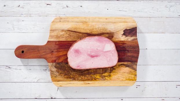 Flat lay. Cutting organic honey ham on a wood cutting board.