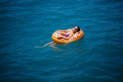 Beautiful young woman in the sea swims on an inflatable ring and has fun on vacation. Girl in a bright swimsuit at the sea under the sunlight