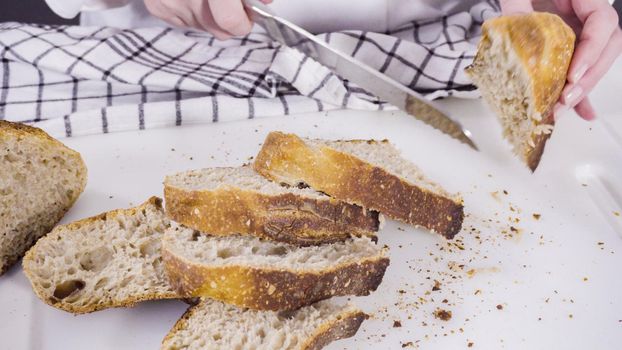 Slicing freshly baked sourdough wheat bread on a white cutting board.