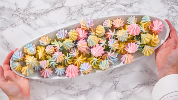 Step by step. Flat lay. Multicolored unicorn meringue cookies on a white serving plate.