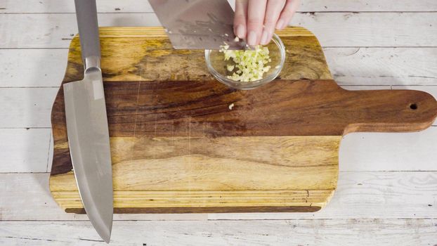 Mincing organic garlic on a wood cutting board.