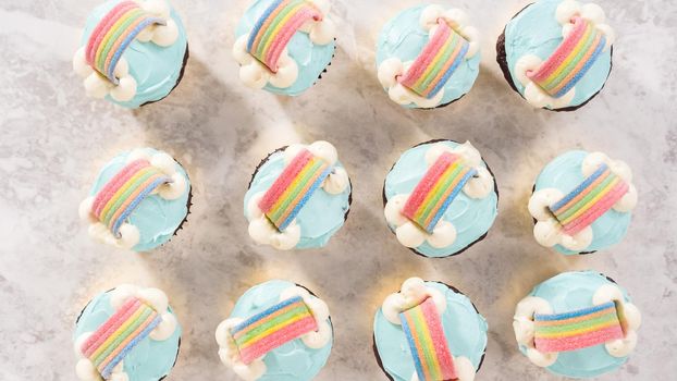 Flat lay. Step by step. Chocolate cupcakes decorated with blue buttercream frosting and rainbow for unicorn theme birthday party.