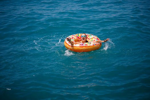 Young woman floating on an inflatable big donut in the transparent turquoise sea. View of a slender lady relaxing on vacation in Turkey, Egypt, Mediterranean Sea.