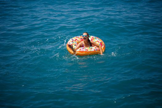 Young woman floating on an inflatable big donut in the transparent turquoise sea. View of a slender lady relaxing on vacation in Turkey, Egypt, Mediterranean Sea.