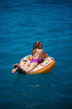 Beautiful young woman in the sea swims on an inflatable ring and has fun on vacation. Girl in a bright swimsuit at the sea under the sunlight