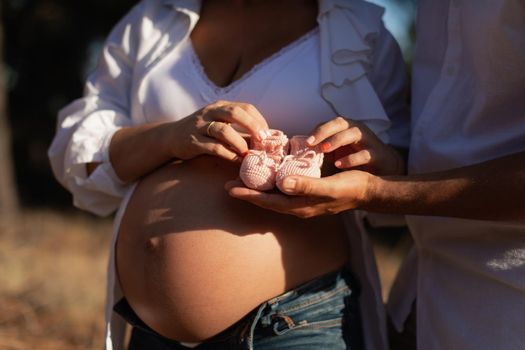 Close-up portrait of a pregnant woman and her husband holding a pair of crochet baby booties in the park during sunset