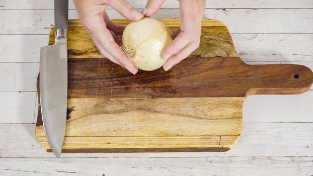 Mincing organic yellow onion on a wood cutting board.