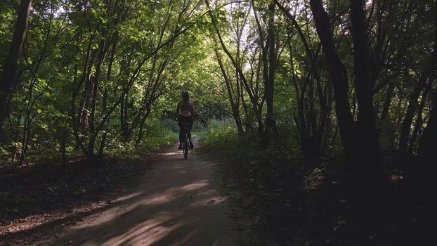 Aerial shot of young sexy sport woman rides bicycle on forest road at summer sunset. Happy holiday or workout on sunny summer day. Healthy cycling lifestyle. 4k slow motion 60 fps